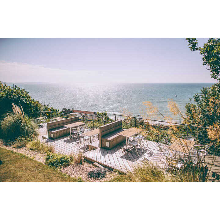 Deck overlooking the sea with tables and chairs, surrounded by greenery.