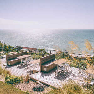 Deck overlooking the sea with tables and chairs, surrounded by greenery.