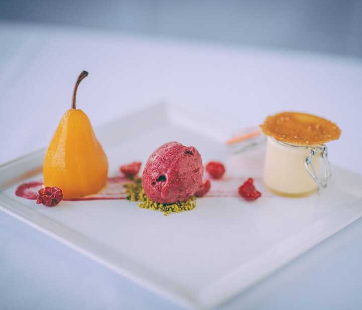 A dessert plate with a yellow pear, raspberry sorbet, and a small pudding.