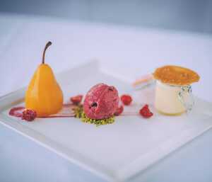 A dessert plate with a yellow pear, raspberry sorbet, and a small pudding.