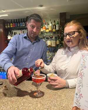 A bartender pours a drink while a woman decorates a cocktail at a bar.