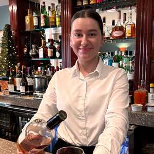 Bartender in a white shirt pouring a drink at a bar with shelves of liquor behind.