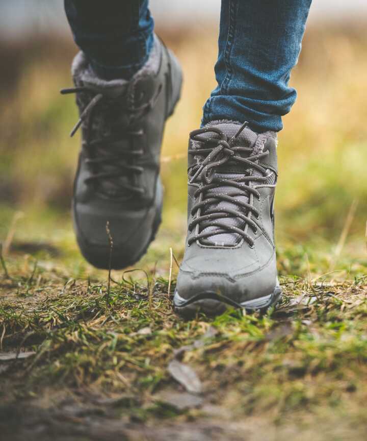 Person walking in gray hiking boots on grassy ground.