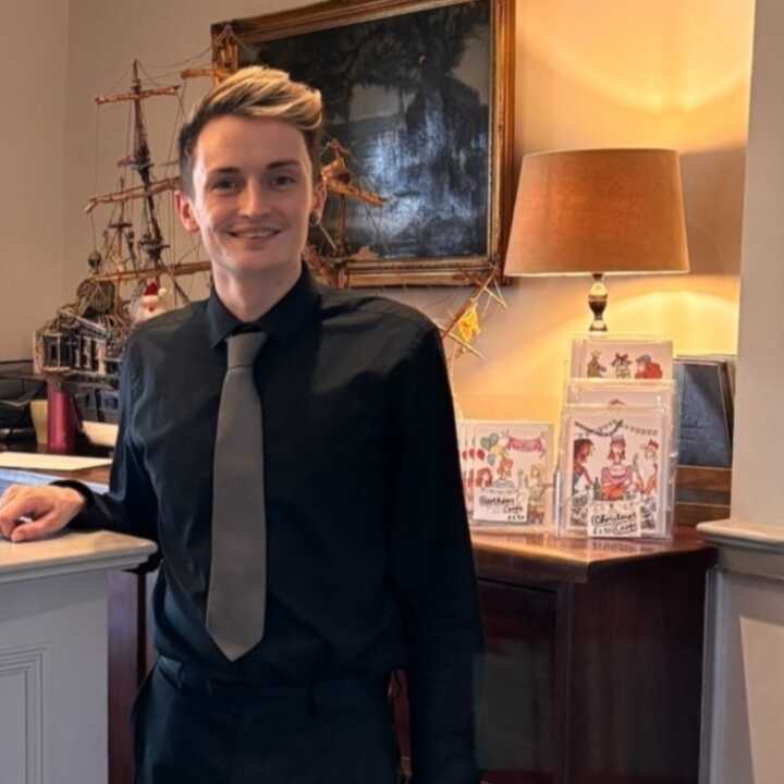 A young man in a black shirt and tie stands in a reception area
